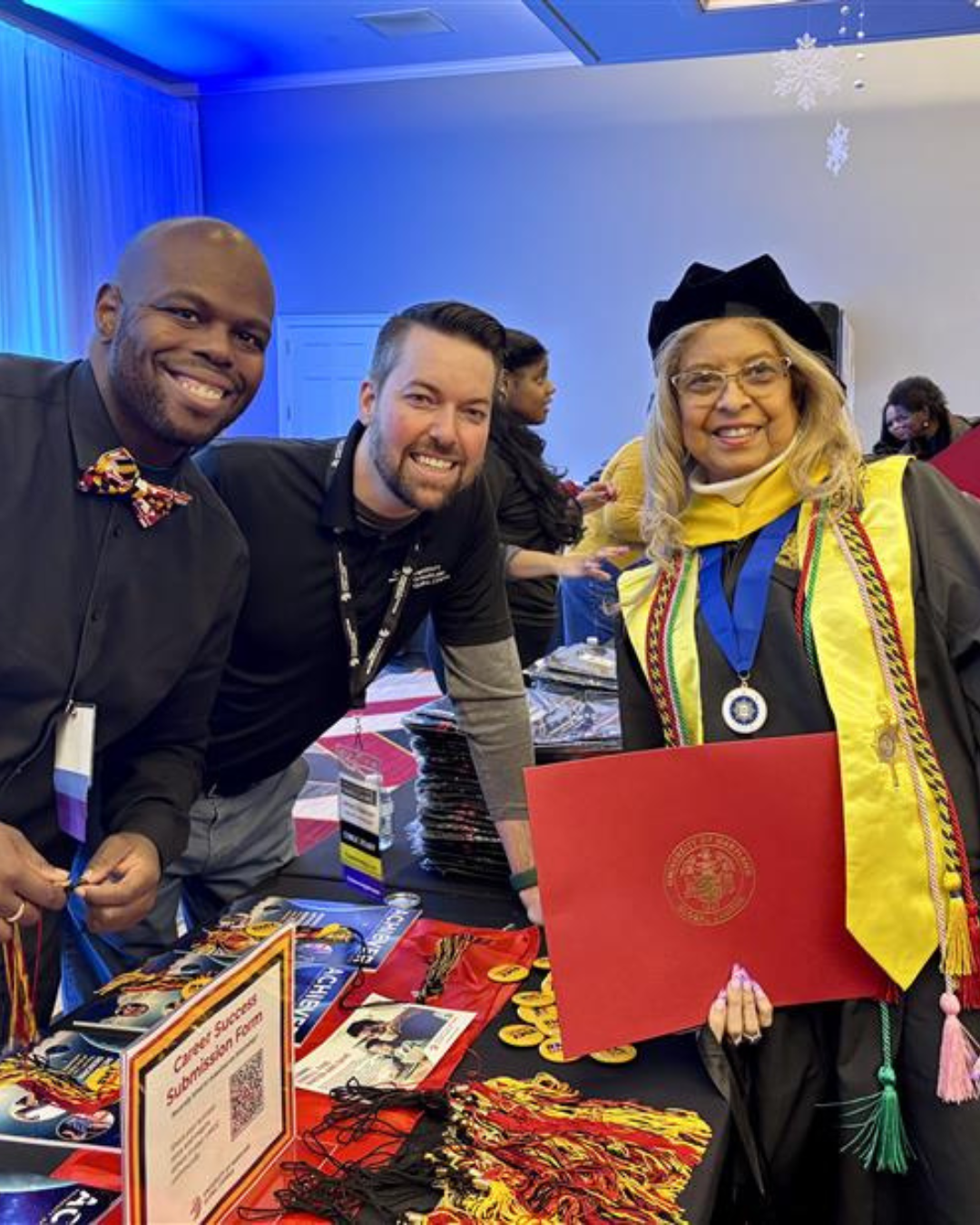 A UMGC alumna in regalia celebrating with two others