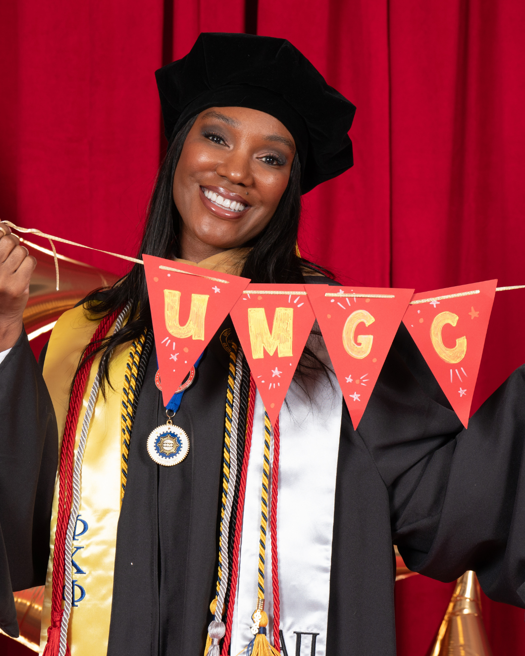 UMGC alum at graduation smiling holding "UMGC" banner