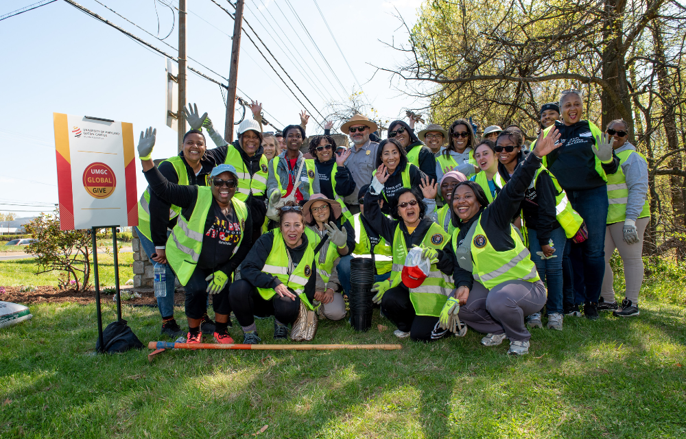 UMGC community members posing in front of the Greenbelt Park sign as they work to plant flowers around the sign